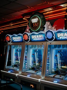 A close-up of colorful pearl fishery arcade machines illuminated by neon lights in an indoor gaming arcade.