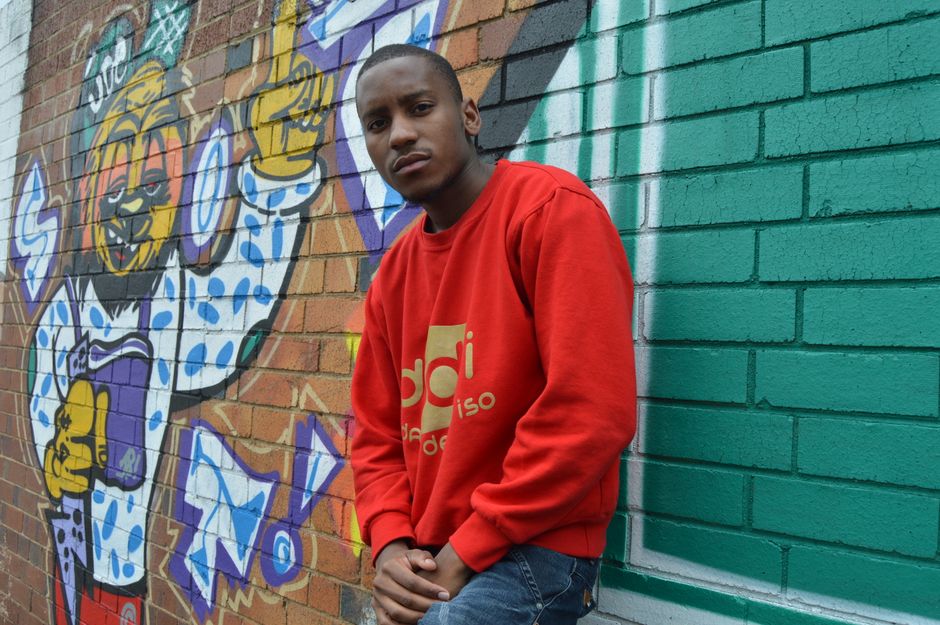 Young man in red sweatshirt poses by vibrant graffiti wall, showcasing urban street style.