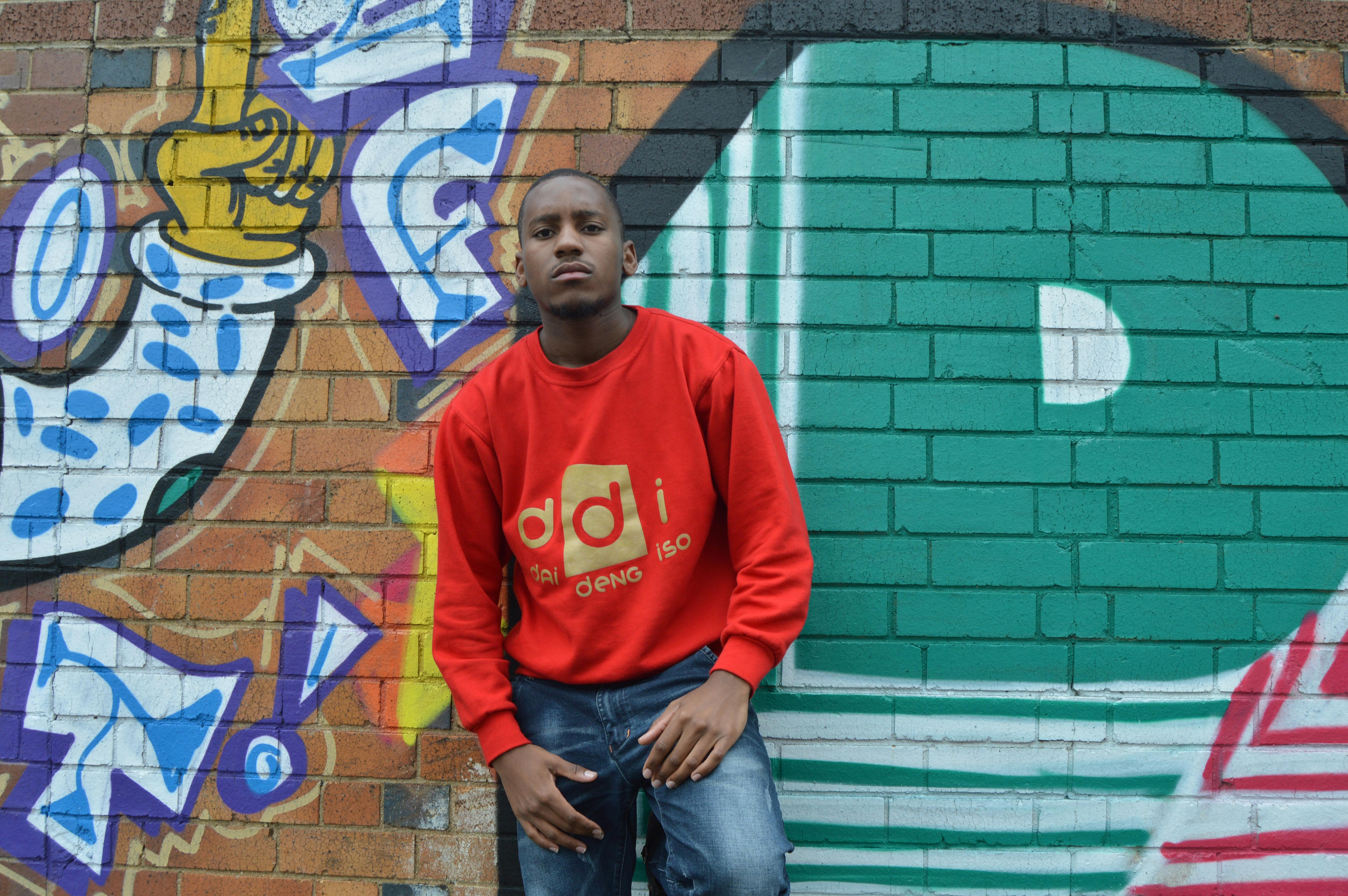 Young man poses in red pullover against vibrant graffiti wall, showcasing urban style.