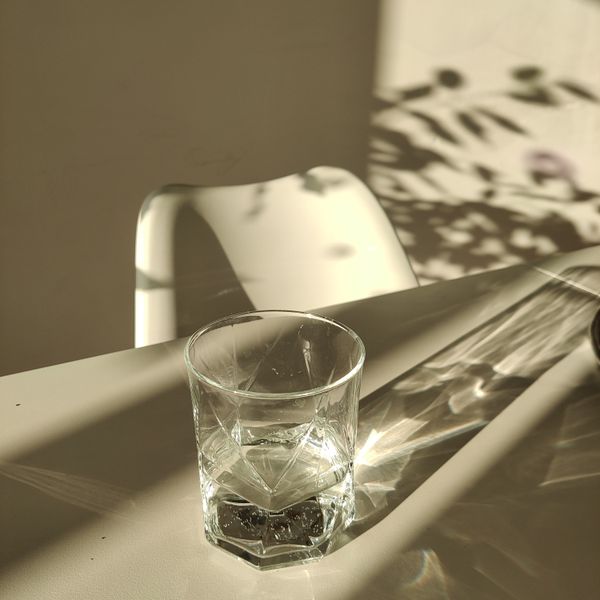 A glass of water throwing shadows across a sunlit table — photo by Elena Galas on Pexels