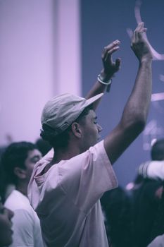 A young adult in a crowd raises arms in celebration or worship, capturing a moment of communal joy.