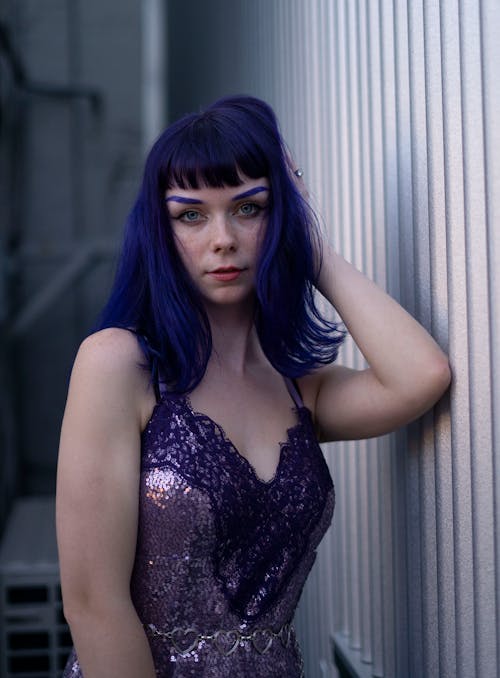 Young Woman with Blue Hair and Eyebrows Posing in a Violet Lace Sequin Dress