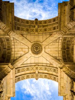 Underneath view of Rua Augusta Arch with detailed stonework and a bright sky in Lisbon, Portugal.