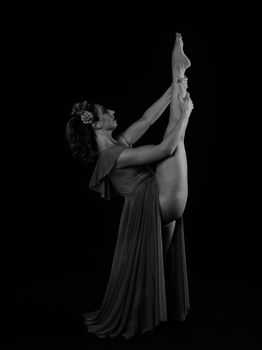 Black and white photo of a woman posing elegantly in a graceful dance position with a black background.
