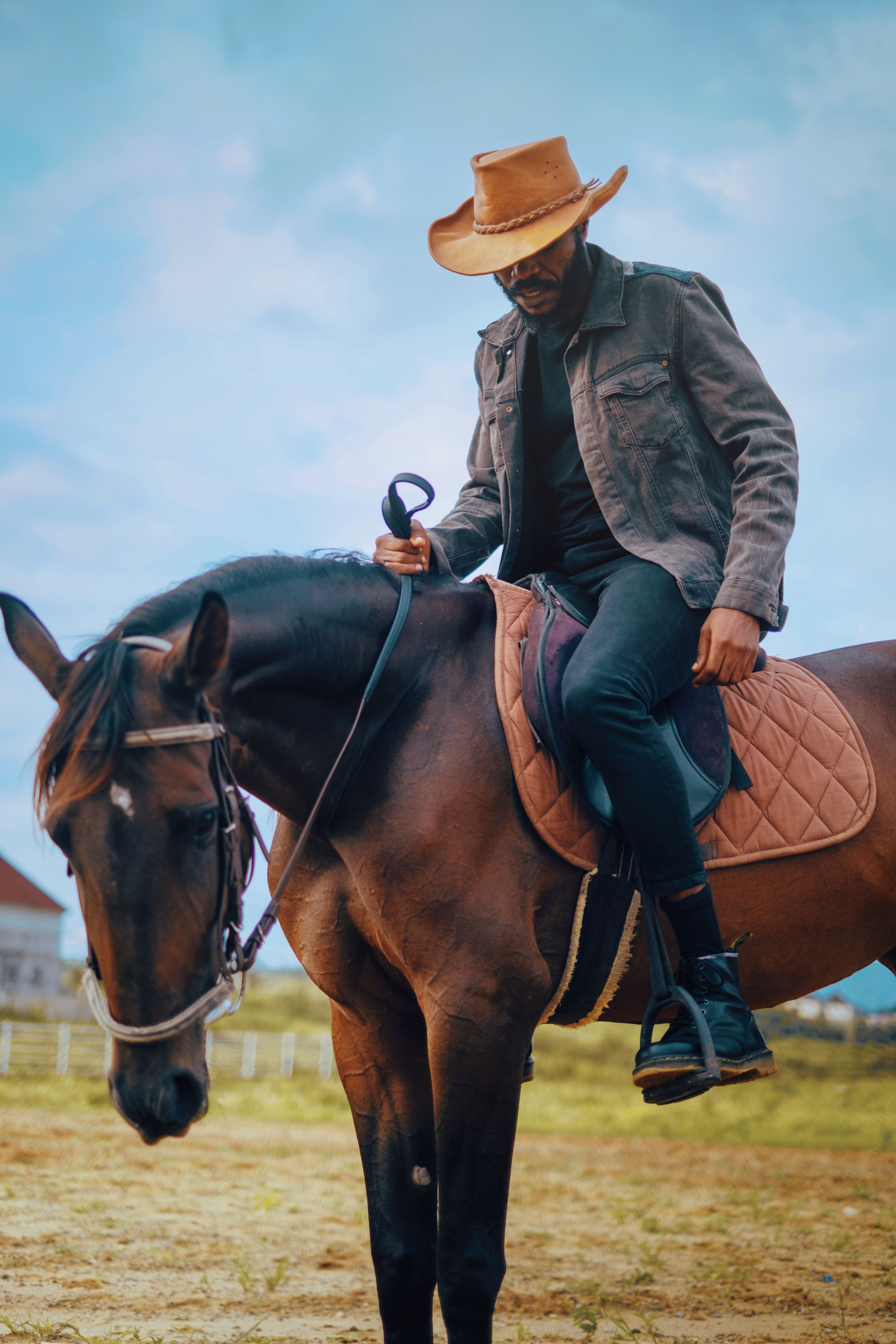 A man wearing a stetson hat horseback riding outdoors in a rural area of Abuja, Nigeria.