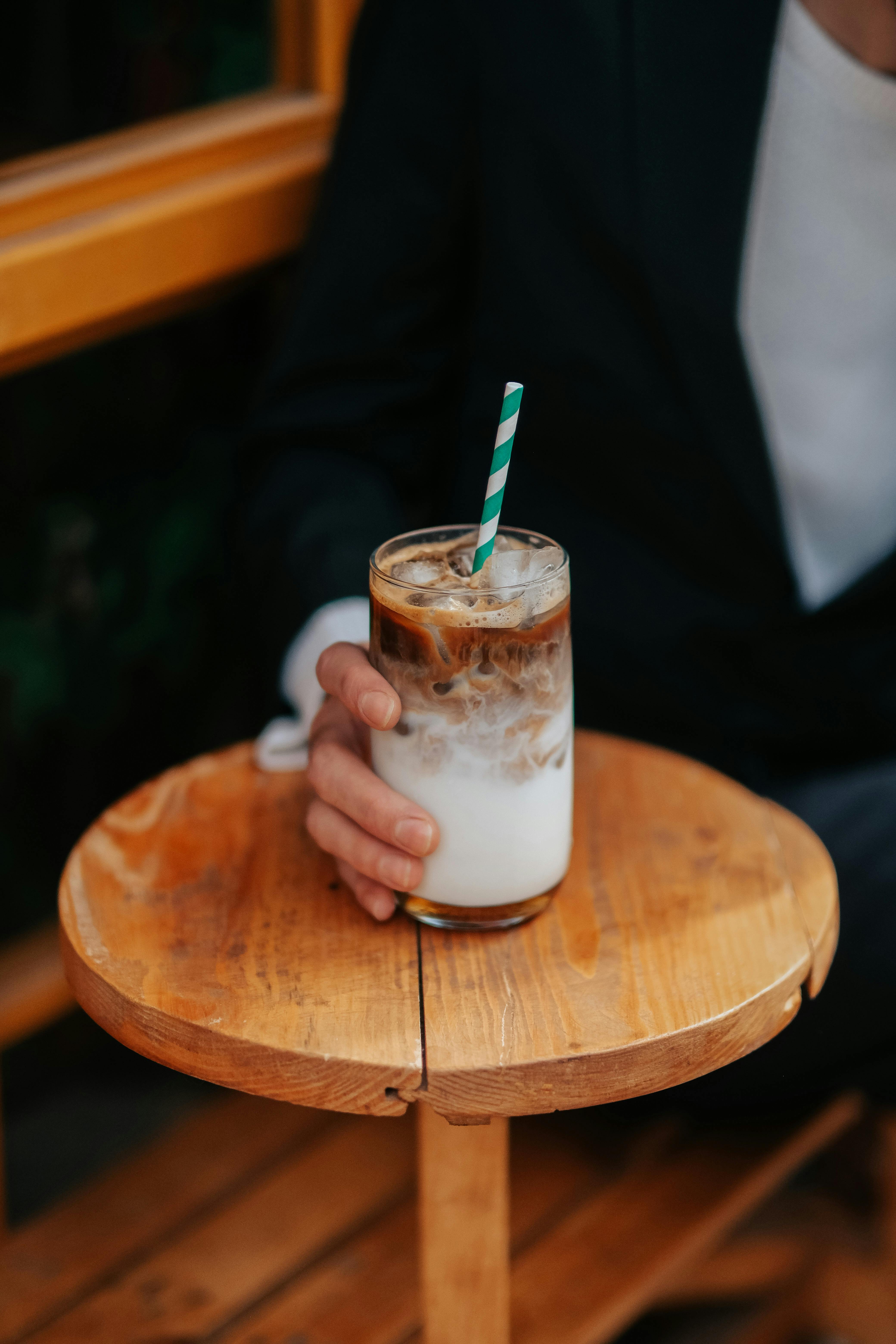 Close-up of iced coffee with a straw in hand on a wooden table, perfect for lifestyle and cafe themes.