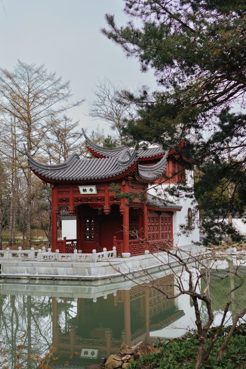 Free A serene view of a traditional Chinese pagoda reflected in a peaceful pond surrounded by trees. Stock Photo