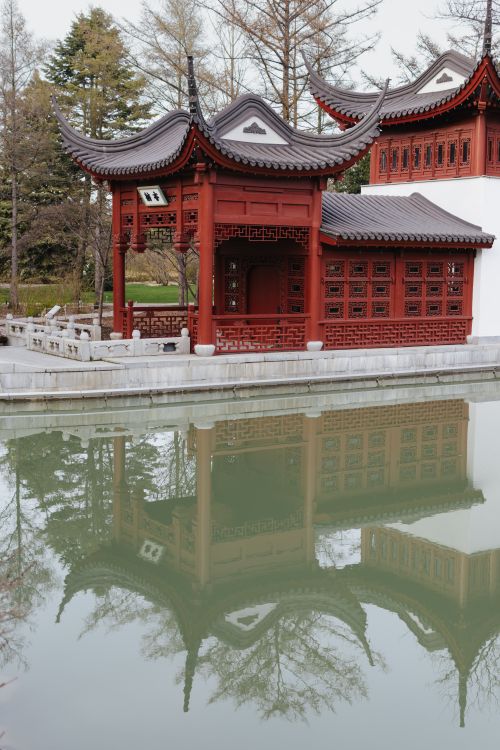 Free A traditional Asian temple reflecting in a tranquil pond surrounded by trees, capturing cultural serenity. Stock Photo