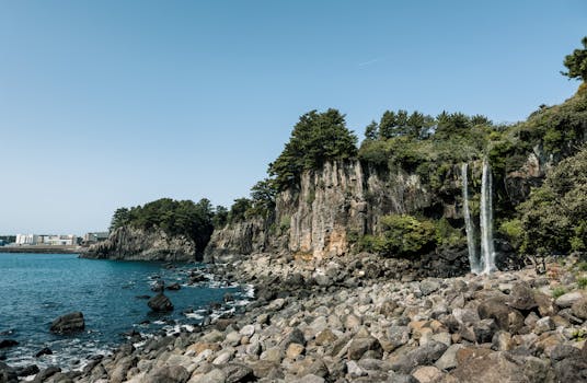 Serene coastal scene of Jeongbang Waterfall in Jeju Island, with rocky shore and blue ocean under a clear sky.