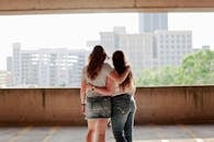 在城市天际线的背景下，两名穿着休闲服装的女性拥抱在一起