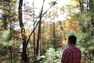 一名穿着红色格子衬衫的男子在秋季阳光普照的森林里平静地散步