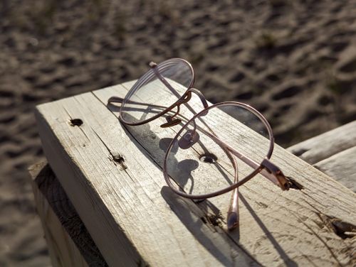 Free Close-up of vintage eyeglasses resting on a sunlit wooden plank at the beach, capturing a serene summer vibe. Stock Photo
