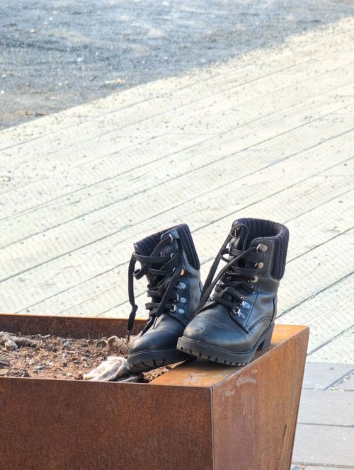 Free Black boots resting on a rusted planter against a wooden boardwalk in Halifax. Stock Photo