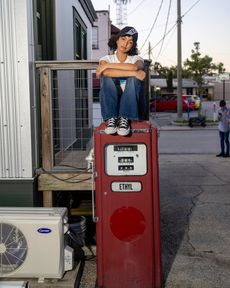 Girl In Baseball Cap Sitting On Retro Gas Pump