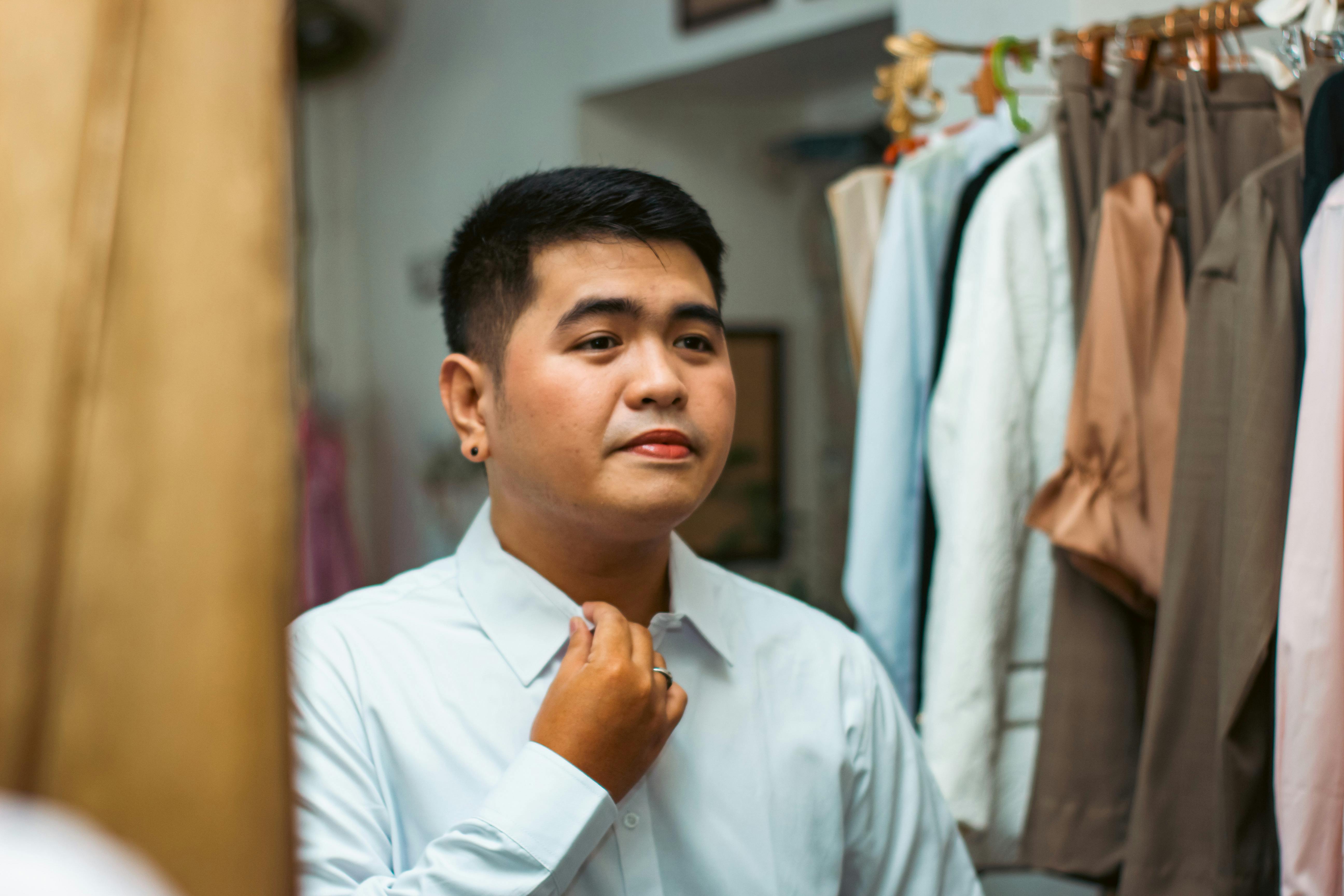 An Asian man in a clothing store adjusting his shirt, preparing for the day.