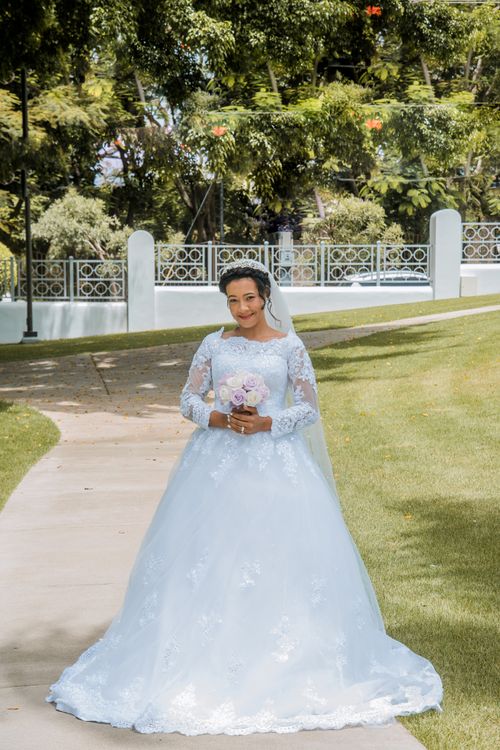 Free A bride in a beautiful white wedding dress holding a bouquet, standing in a park in Santo Domingo. Stock Photo