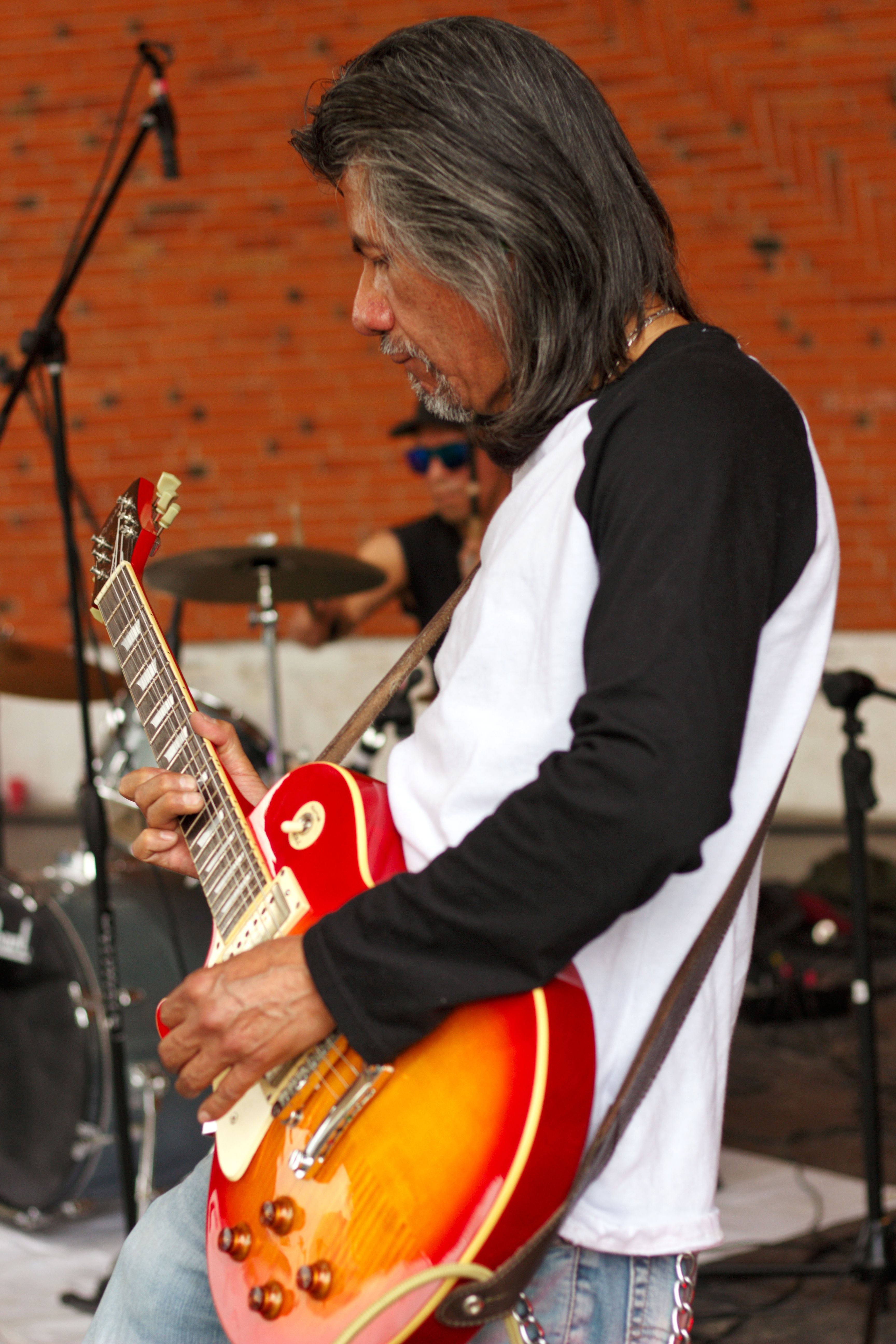 Musician playing electric guitar at concert with visible drums and microphone.