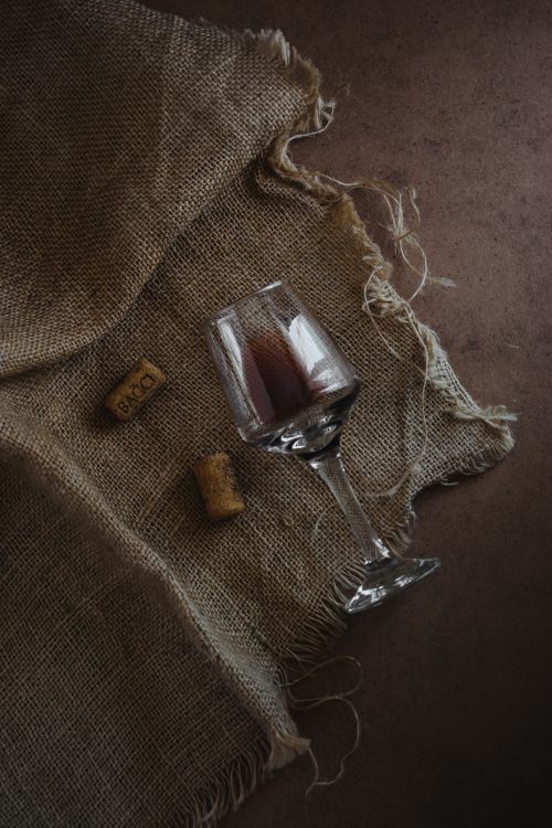 Free An elegant glass of red wine on a rustic linen cloth with wine corks, creating a vintage ambiance. Stock Photo