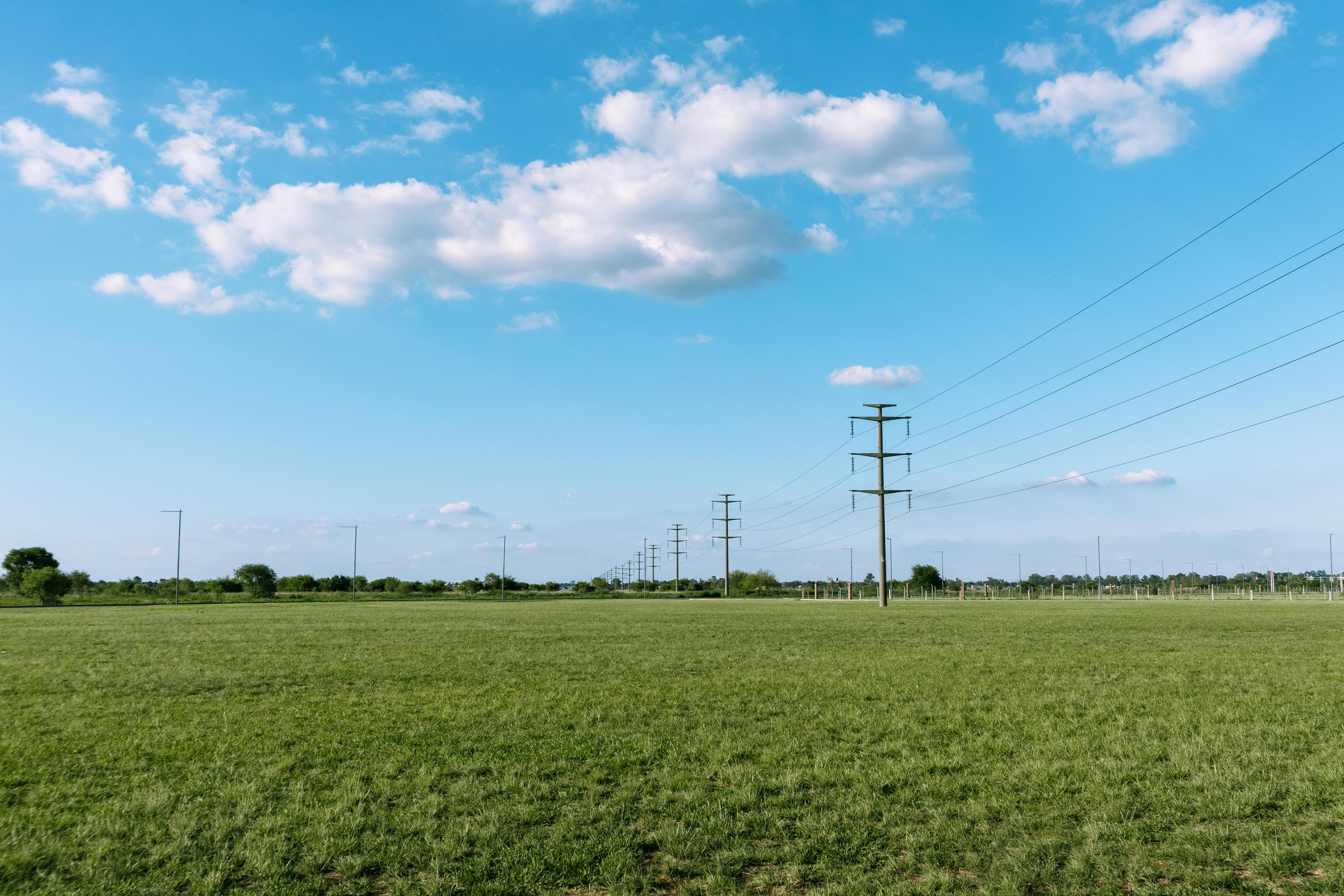 Tranquil rural scene with green field, utility poles, and blue sky in Rosario, Argentina.