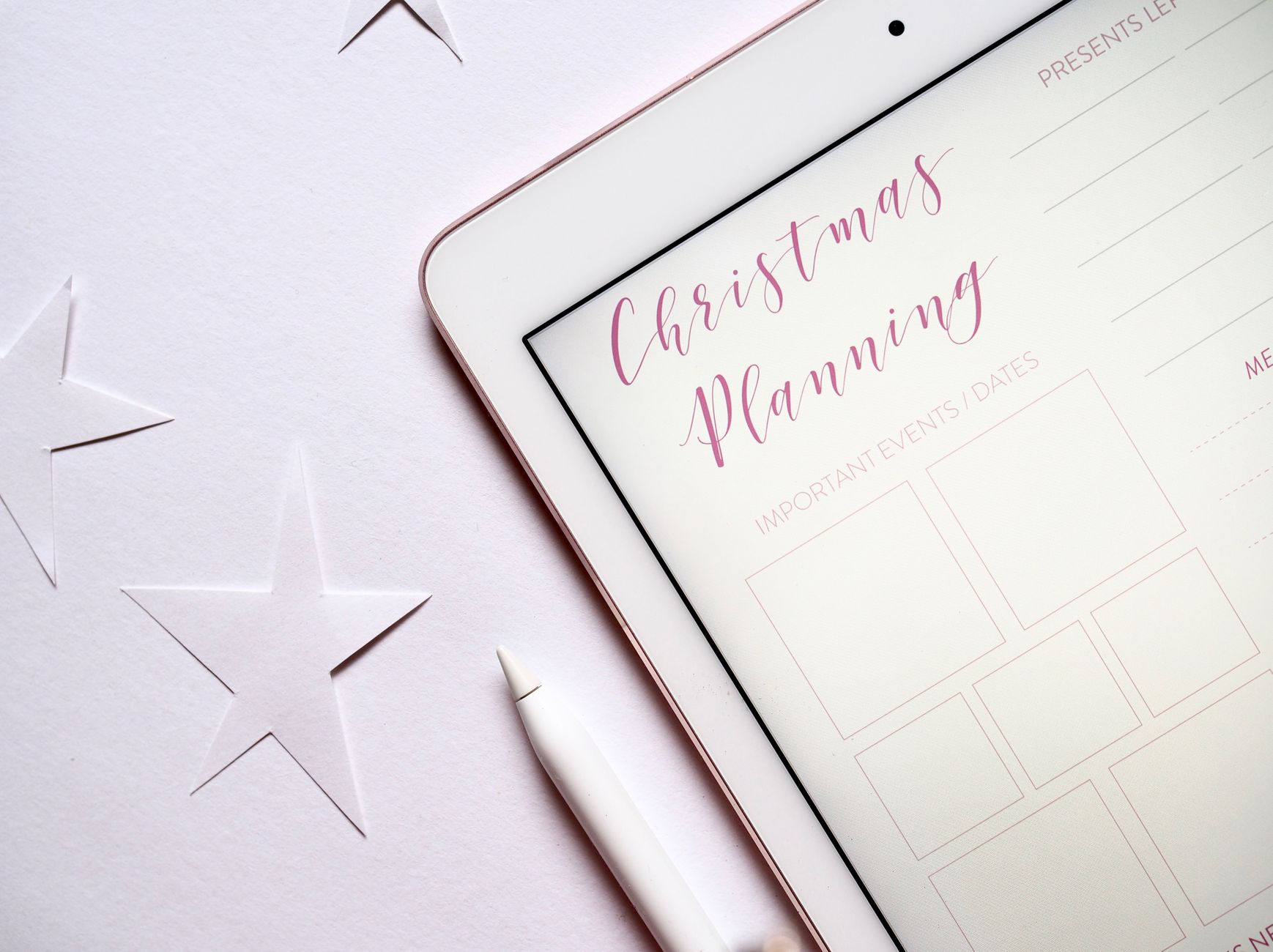 Top view of a tablet with Christmas planning template and stars on a white surface.