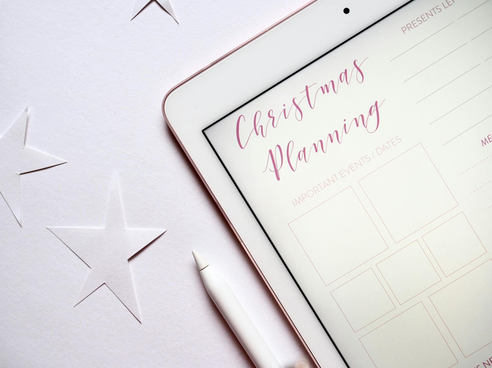 Top view of a tablet with Christmas planning template and stars on a white surface.