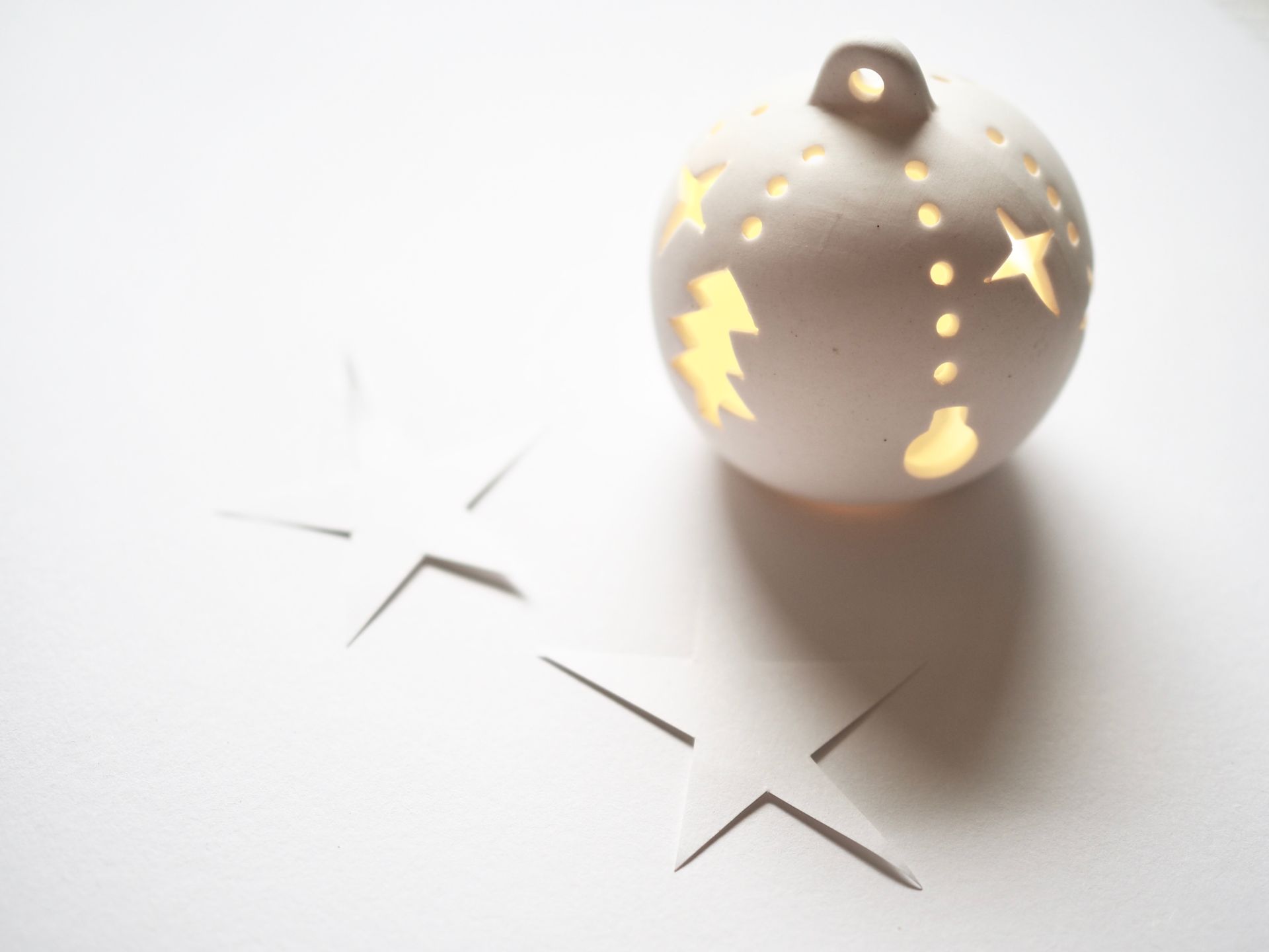 Close-up of a glowing Christmas ornament with star cutouts on a white background.