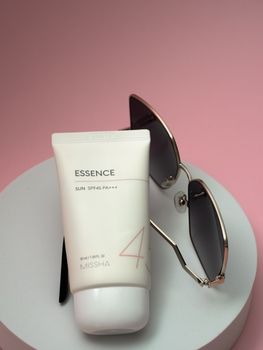 Flat lay of SPF 45 sunscreen and sunglasses on a pink backdrop, highlighting summer essentials.