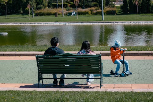 Couple Sitting on a Bench and a Child Playing on a Kick Scooter 