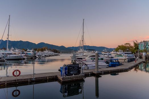 Scenic view of a marina in Vancouver, BC, at sunset with yachts and mountains in the background.