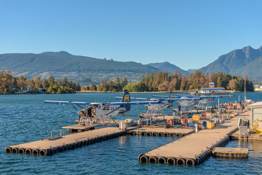 Scenic view of seaplanes docked at a pier in Vancouver, BC, with mountain backdrop.
