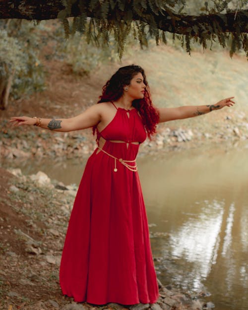 Young Woman in a Long Red Dress Posing by the Lake 