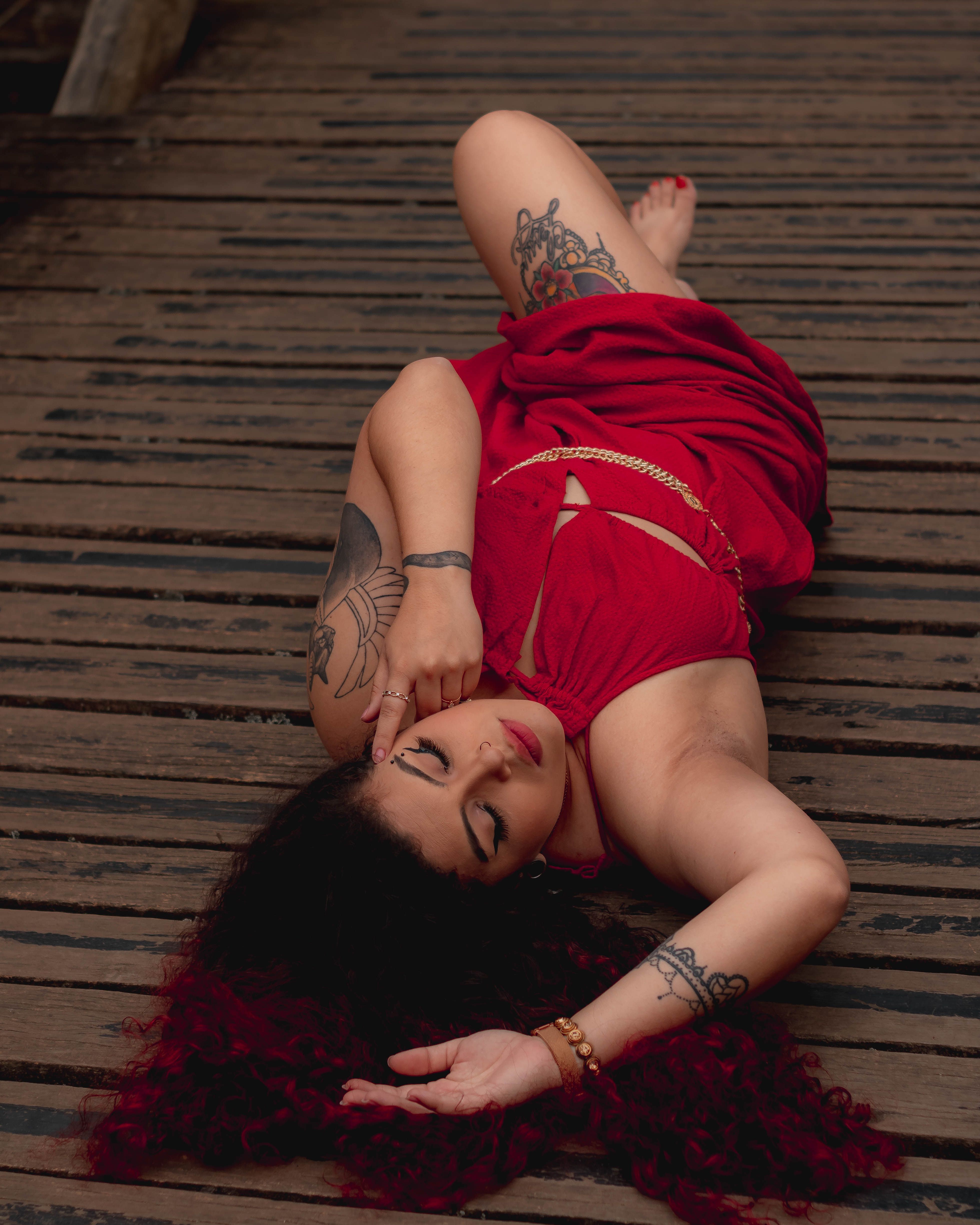 Young Woman in a Long Red Dress Lying on Wooden Surface · Free Stock Photo