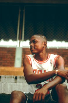 Portrait of a young basketball player in a jersey sitting outdoors on a court.