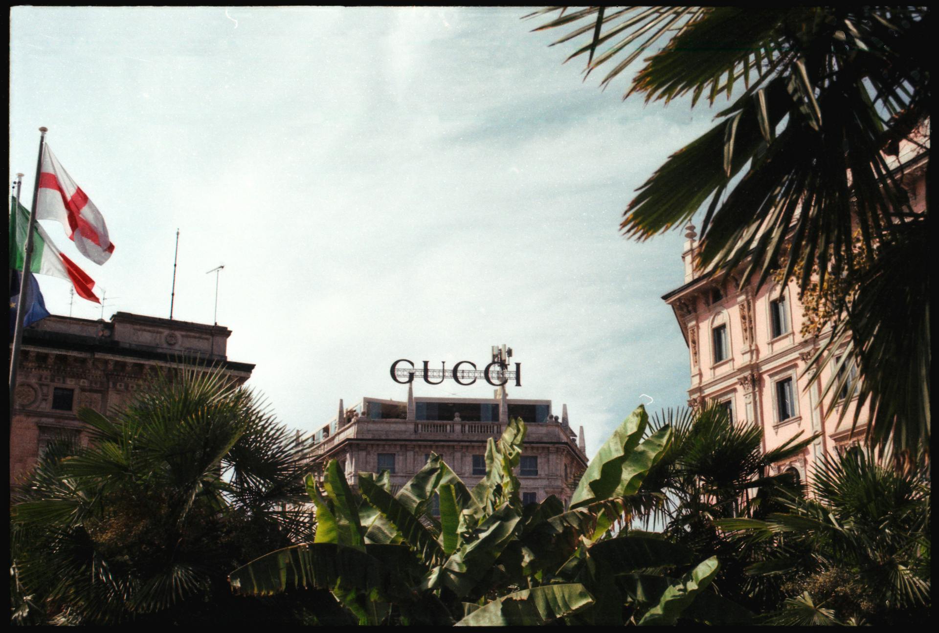 View of Gucci store amidst lush palm trees and historic buildings in Milan, Italy.