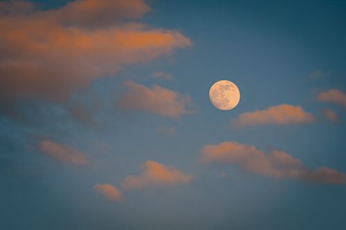 Free Capture of a full moon surrounded by colorful clouds at sunset. Stock Photo
