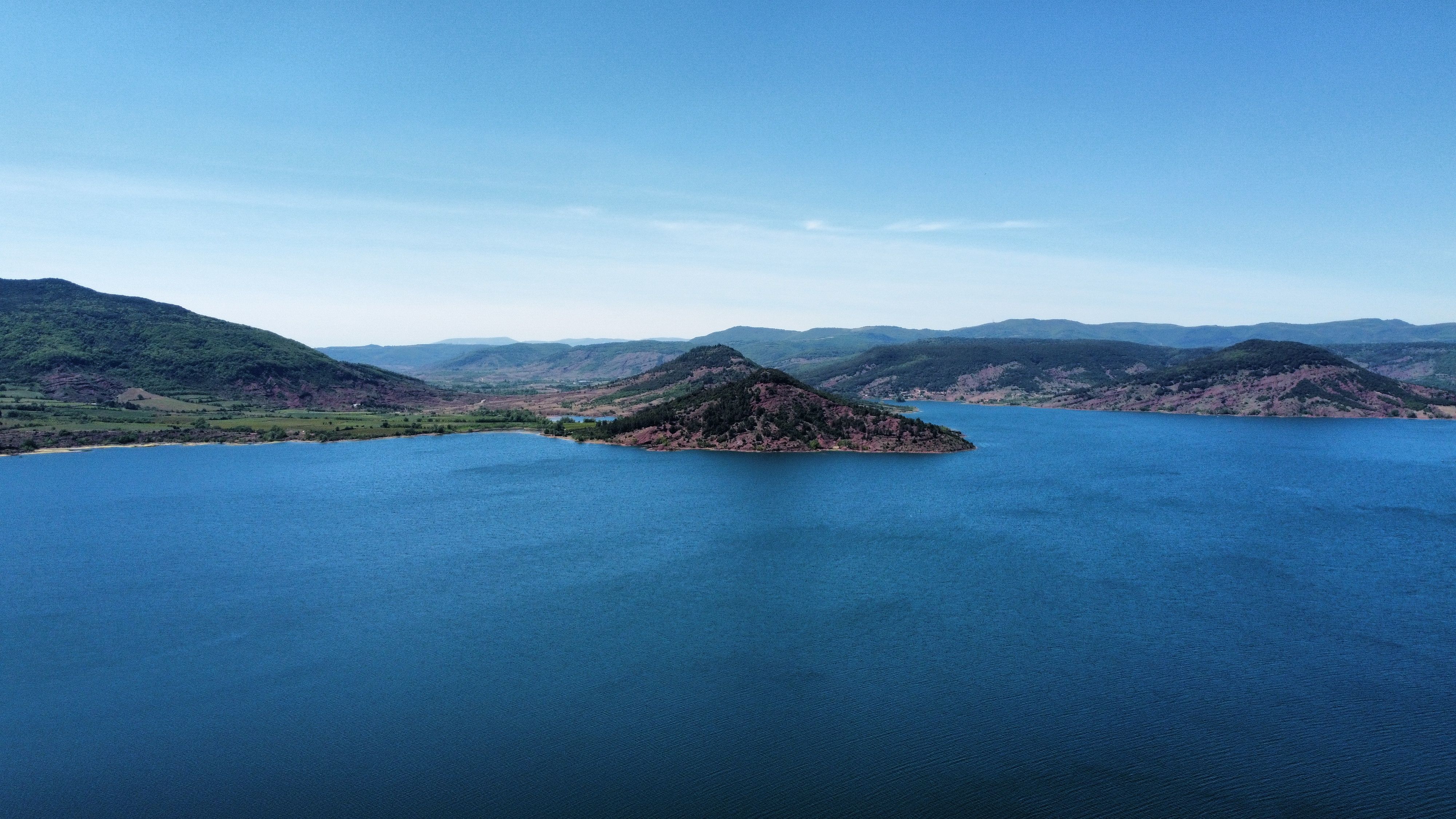 Aerial view of a tranquil lake surrounded by scenic hills in Clermont-l'Hérault, Occitanie, France.
