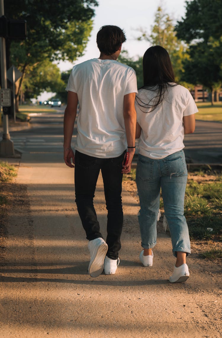 Young Couple In White T-shirts And Trainers Walking On Suburban Street