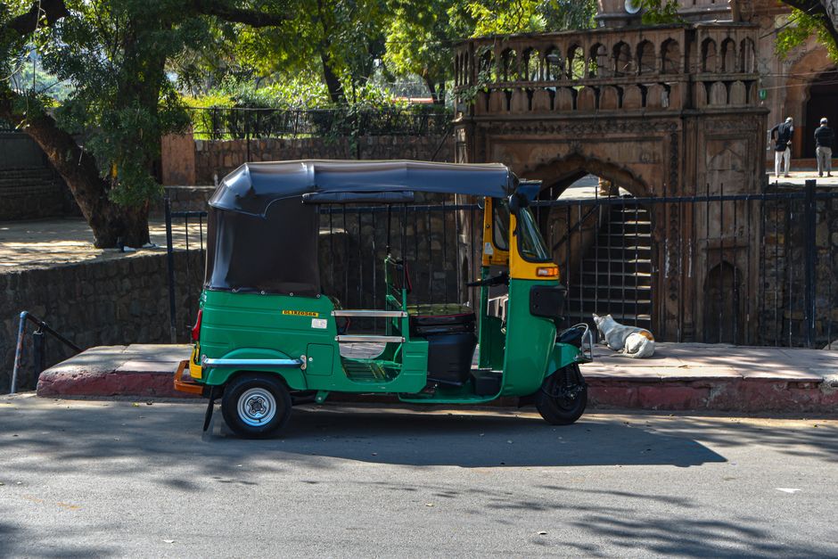 Colorful auto-rickshaw navigating a busy street in Delhi, India.