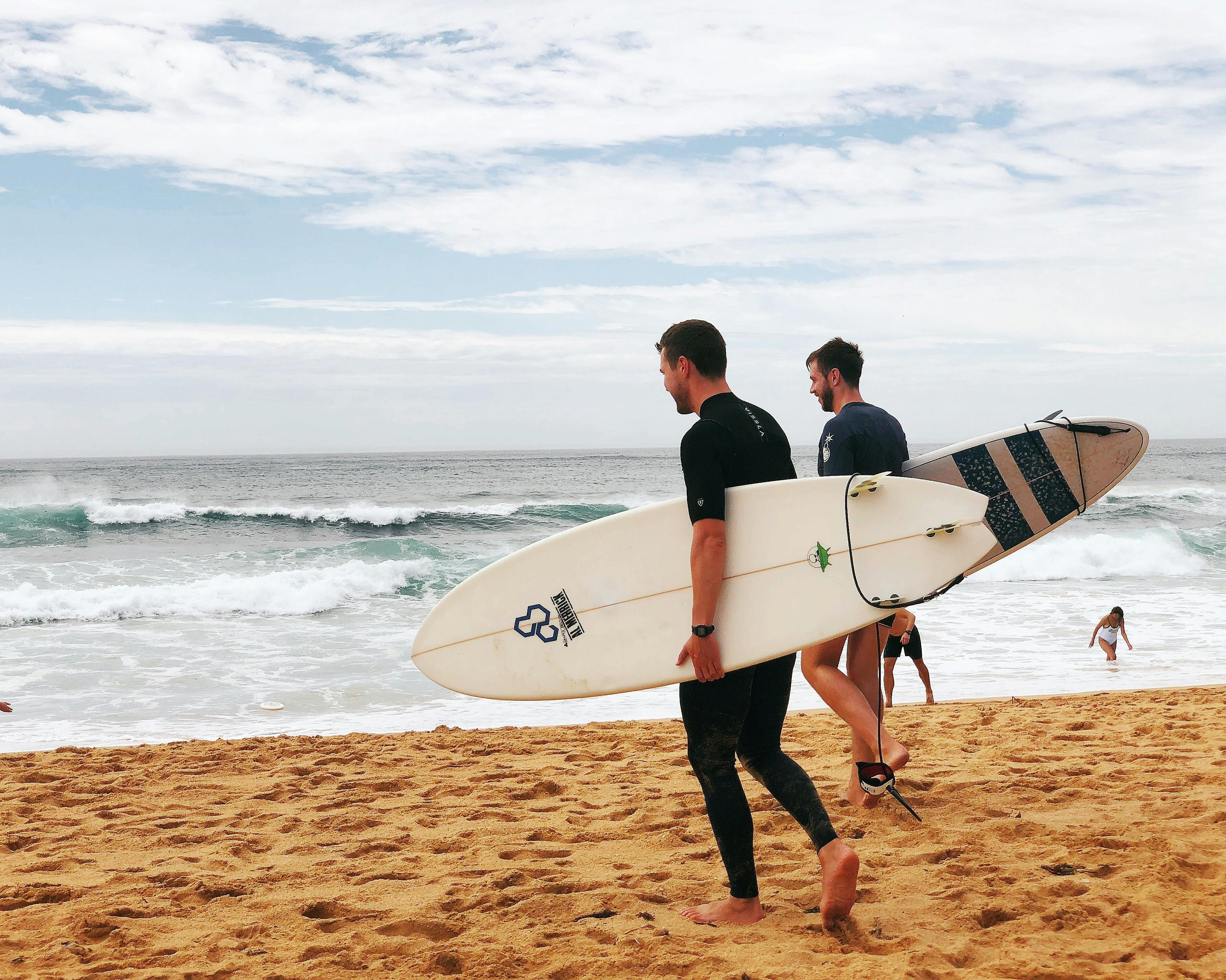 two men carrying surfboards near seashore