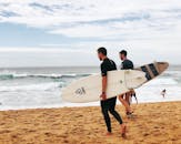 两名男子手持冲浪板，沿着新南威尔士州的阿沃卡海滩行走，捕捉着澳大利亚海岸的夏日精髓