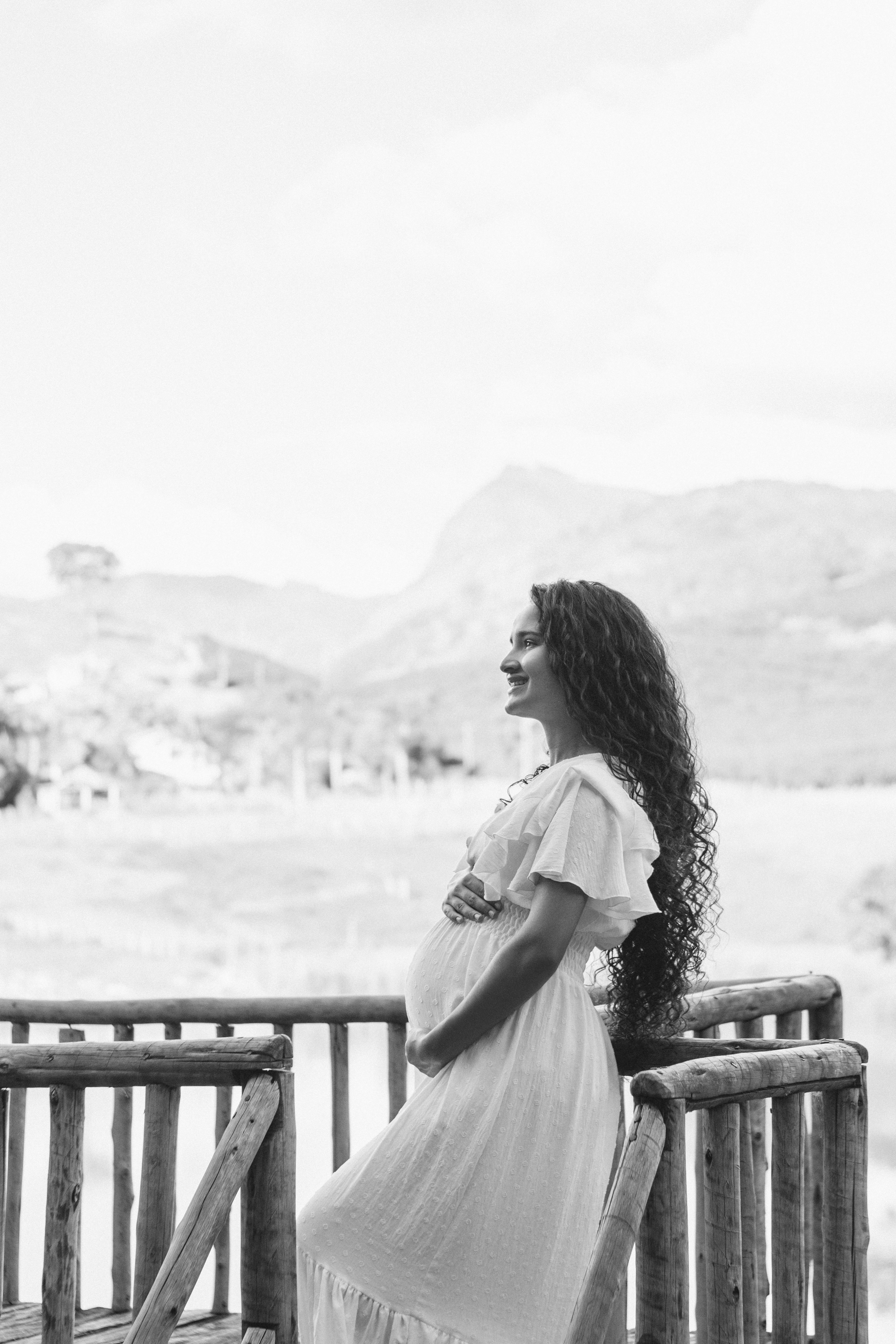 Black and white photo of a smiling pregnant woman standing on a rustic terrace outdoors.
