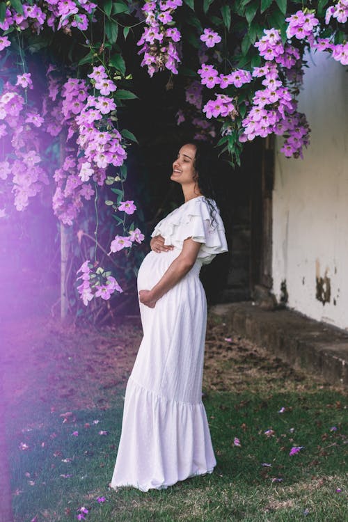 Pregnant Woman in a White Dress under a Tree in Blossom 