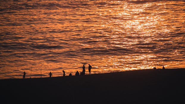 Silhouetted people enjoying a peaceful sunset at Punta Hermosa, Peru, with golden ocean reflections.