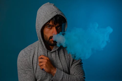 Studio Shot of a Man Wearing a Hood Smoking an Electronic Cigarette 