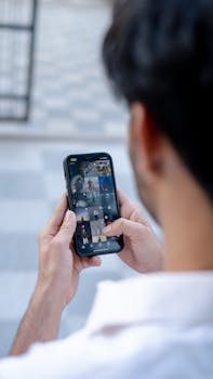 A man views photos on his smartphone while standing outside, holding the device with both hands.