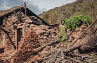 印度农村发生一场灾难后，一名妇女站在被毁的房屋前，描绘着挣扎