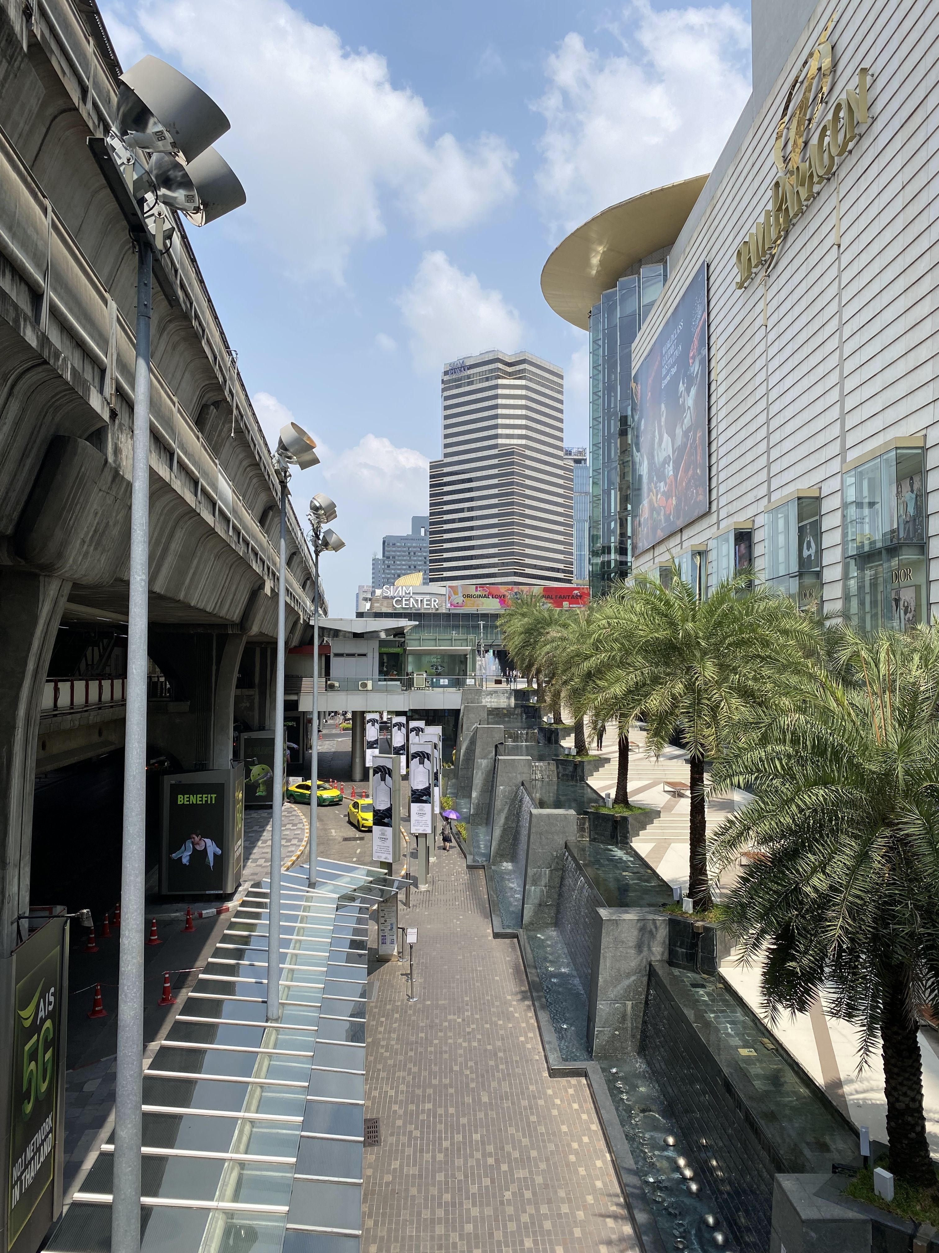 Sunlit cityscape featuring modern buildings, palm trees, and shopping mall.