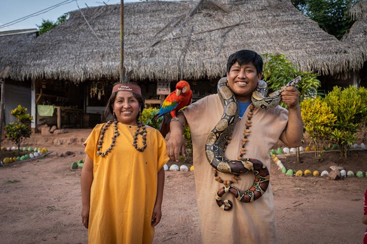 Smiling Man And Woman Standing Outside And Holding A Parrot And A Snake 