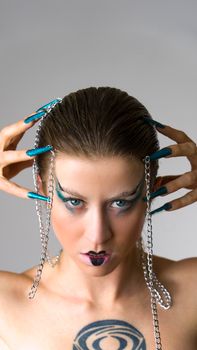 Striking studio portrait of a woman with bold makeup, chains, and tattoos on a neutral backdrop.