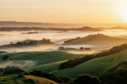 A sunrise over a valley with fog and hills